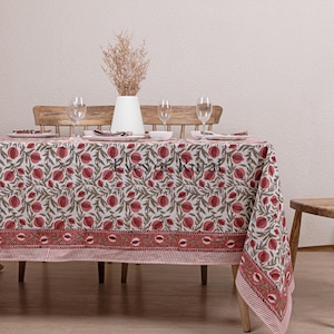 Peut inclure: Une nappe blanche avec un motif floral rouge et vert. La nappe est posée sur une table en bois avec quatre couverts. Il y a des verres, des assiettes et des serviettes sur la table.