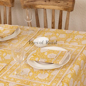 May include: A yellow and white floral tablecloth with a white bowl and two glasses on top. The tablecloth has a border of white and yellow stripes. The text "Eyes of Rural" is visible in the center of the image.