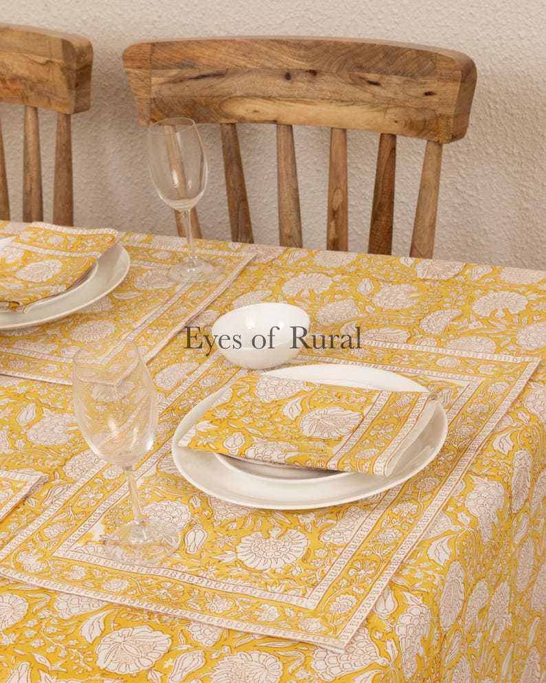 May include: A yellow and white floral tablecloth with a white bowl and two glasses on top. The tablecloth has a border of white and yellow stripes. The text "Eyes of Rural" is visible in the center of the image.
