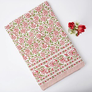 May include: White cotton tablecloth with a red and green floral print. The tablecloth has a border with a repeating floral pattern.