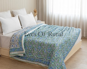 May include: A blue floral quilt with a white border is draped over a bed. The quilt features a repeating pattern of blue flowers and green leaves. White pillows are arranged on the bed, and the text "Eyes Of Rural" is visible.