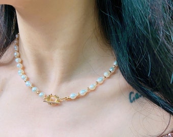 Colar gargantilha com pérolas douradas, fecho em forma de margarida e contas de pérola barroca.