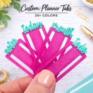 May include: A set of bright pink planner tabs with teal lettering. The tabs feature the words notes, today, month, and todo in a cursive font. The text Custom Planner Tabs 30+ COLORS is printed above the tabs in a black script and sans-serif font.