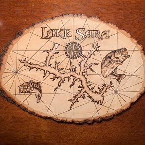 May include: A wooden sign with a map of Lake Sara, a compass, and two bass fish. The sign is burned with the words "Lake Sara" at the top.