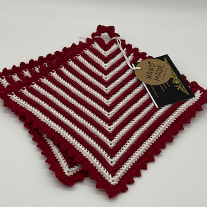 Könnte beinhalten: Zwei rot-weiß gestreifte gehäkelte Topflappen mit einem gewellten Rand. Die Topflappen haben einen Schlaufe-Griff und ein braunes Etikett mit der Aufschrift "HANDMADE" in weißen Buchstaben.