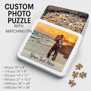 May include: A custom photo puzzle with a matching tin. The puzzle features a romantic beach scene with a couple embracing at sunset. The tin is open, revealing the assembled puzzle pieces. Text on the tin reads "Your Text Here". Puzzle sizes range from 30 pieces (10" x 8") to 2000 pieces (40" x 28").