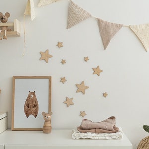 May include: A nursery room decorated with a brown bear print, wooden stars, and a fabric garland. A wooden stacking toy sits on a white surface.