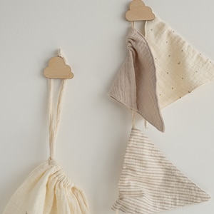 May include: Two wooden cloud-shaped hooks on a white wall with three fabric triangle banners hanging from them. The banners are in shades of beige and brown with different patterns.