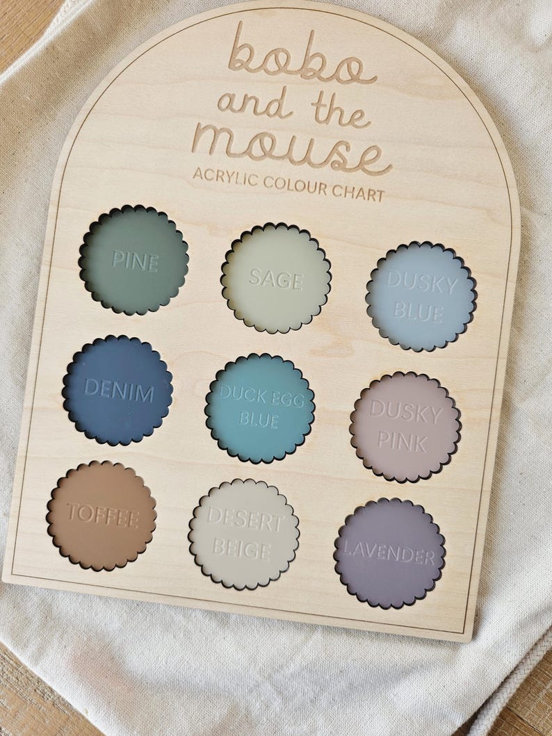 May include: Wooden color chart with nine scalloped acrylic color samples. The colors include Pine, Sage, Dusky Blue, Denim, Duck Egg Blue, Dusky Pink, Toffee, Desert Beige, and Lavender. The text "koko and the mouse" and "ACRYLIC COLOUR CHART" are engraved on the wood.