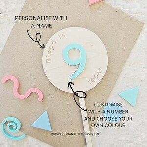 May include: A wooden cake topper with the number 9 in light blue, the word "TODAY" and the name "Pippa" in pink. The text "PERSONALISE WITH A NAME" and "CUSTOMISE WITH A NUMBER AND CHOOSE YOUR OWN COLOUR" are also included.