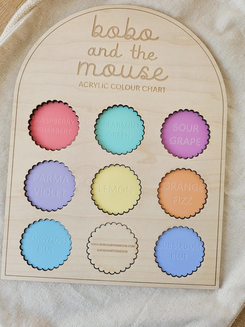 May include: Wooden acrylic color chart by Bobo and the Mouse. The chart features nine scalloped circles with various colors and names, including Raspberry Sherbert, Spearmint Green, and Bubblegum Blue. The brand name is at the top.