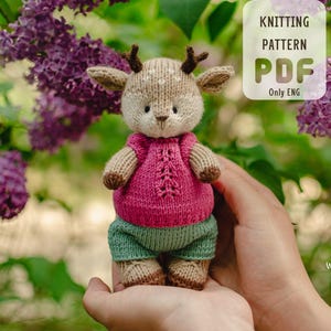Könnte beinhalten: Strickmuster PDF für ein süßes Amigurumi-Spielzeug in Form eines Rehs. Das Reh trägt einen rosa Pullover und eine grüne Hose. Das Muster ist nur in englischer Sprache verfügbar.