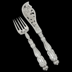 May include: A silver serving set with an ornate design. The fork and knife have intricate details and a floral pattern.