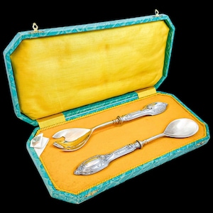 May include: A set of silver salad servers in a green and yellow box. The servers have ornate handles and are in a velvet-lined box.