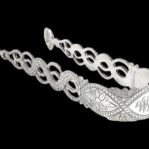 May include: Silver sugar tongs with an ornate design featuring a floral motif and a decorative border. The tongs are made of silver and have a polished finish.