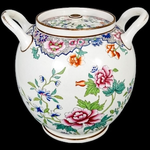 May include: A white porcelain jar with a lid and two handles. The jar is decorated with a floral pattern in shades of pink, blue, green, and orange.
