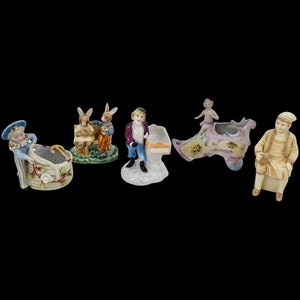 May include: Five porcelain figurines, each with a different design. One features two rabbits sitting on a bench, another a boy holding a tray, a third a girl in a shoe, a fourth a girl in a basket, and the last a man sitting on a bench.