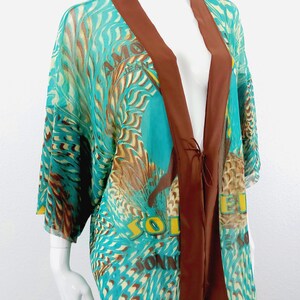 May include: A turquoise and brown sheer kimono with a brown satin trim and tie closure. The kimono has a colorful print of feathers and the words "Soleil" and "Amore" on the front.