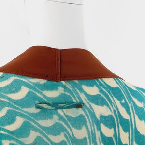 May include: Back view of a teal and white patterned dress with a brown collar. The dress has a small brown loop on the back.