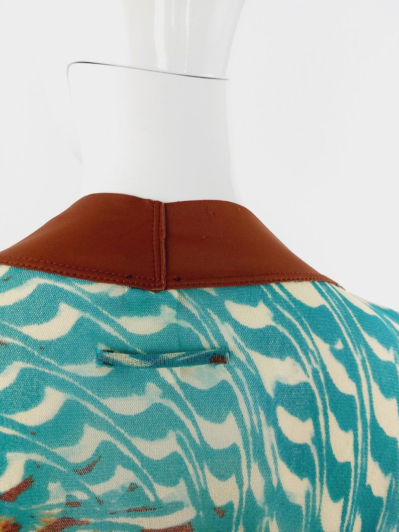 May include: Back view of a teal and white patterned dress with a brown collar. The dress has a small brown loop on the back.