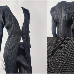 May include: A black pleated trouser suit with a long, open-front jacket. The jacket has a V-neck and padded shoulders. The trousers are straight-leg and have a high waist.