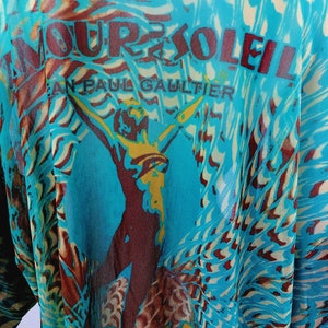 May include: A turquoise blue sheer top with a brown and yellow graphic print of a woman with the text "Amour Soleil Jean Paul Gaultier" on the front.