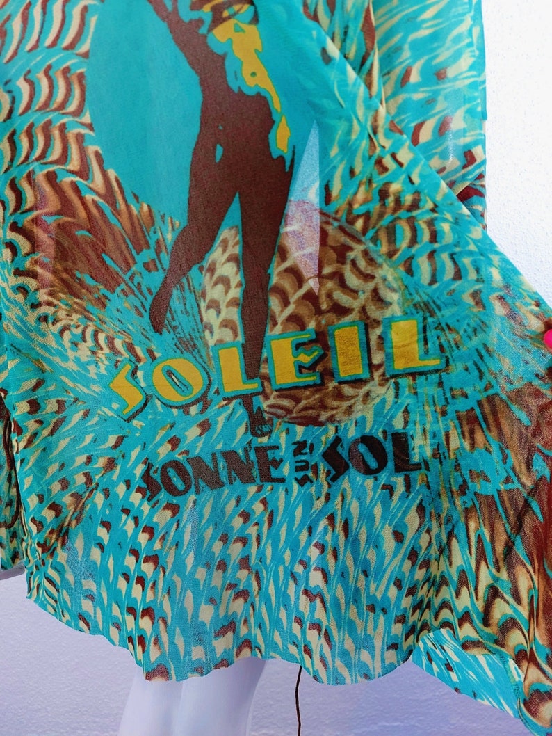 May include: A turquoise blue sheer fabric with a brown silhouette of a person and the words "SOLEIL" and "CONNESOL" printed in yellow.