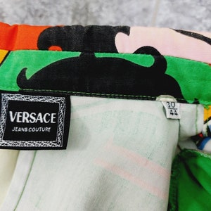 May include: A close-up of a white, green and black patterned fabric with a black label that reads "VERSACE JEANS COUTURE". A smaller white label with black text reads "30 44".
