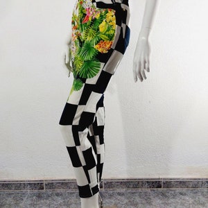 May include: Black and white checkered pants with a tropical floral print on the front. The pants are made of denim and have a high waist.