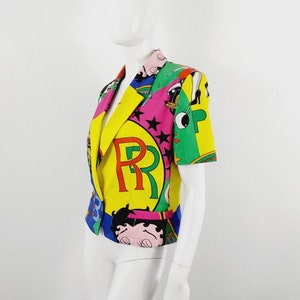 May include: A colourful short-sleeved blazer with a multi-coloured print featuring cartoon characters, stars, and the letters "RR".