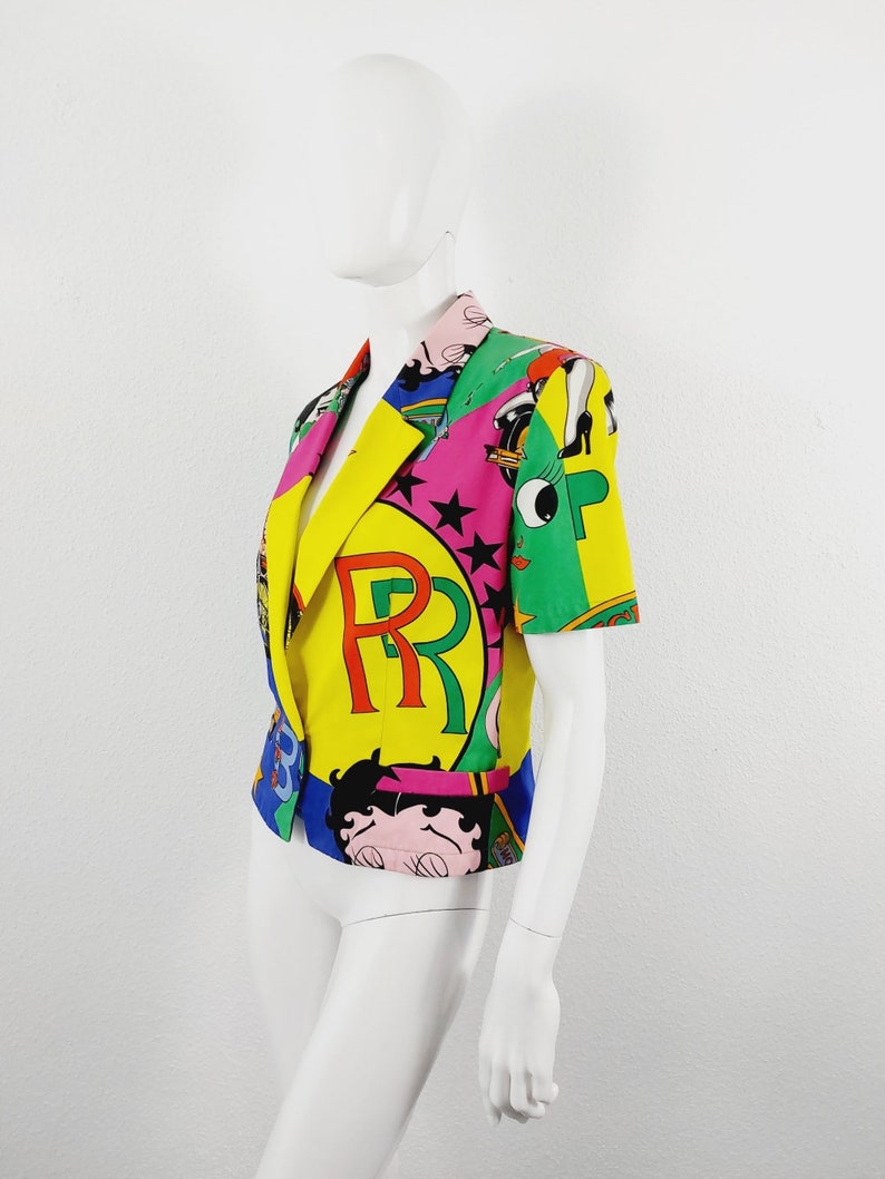 May include: A colourful short-sleeved blazer with a multi-coloured print featuring cartoon characters, stars, and the letters "RR".