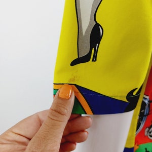 May include: A yellow, blue, green, orange and white patterned fabric with a cartoon image of a woman's leg in a black high-heeled shoe.