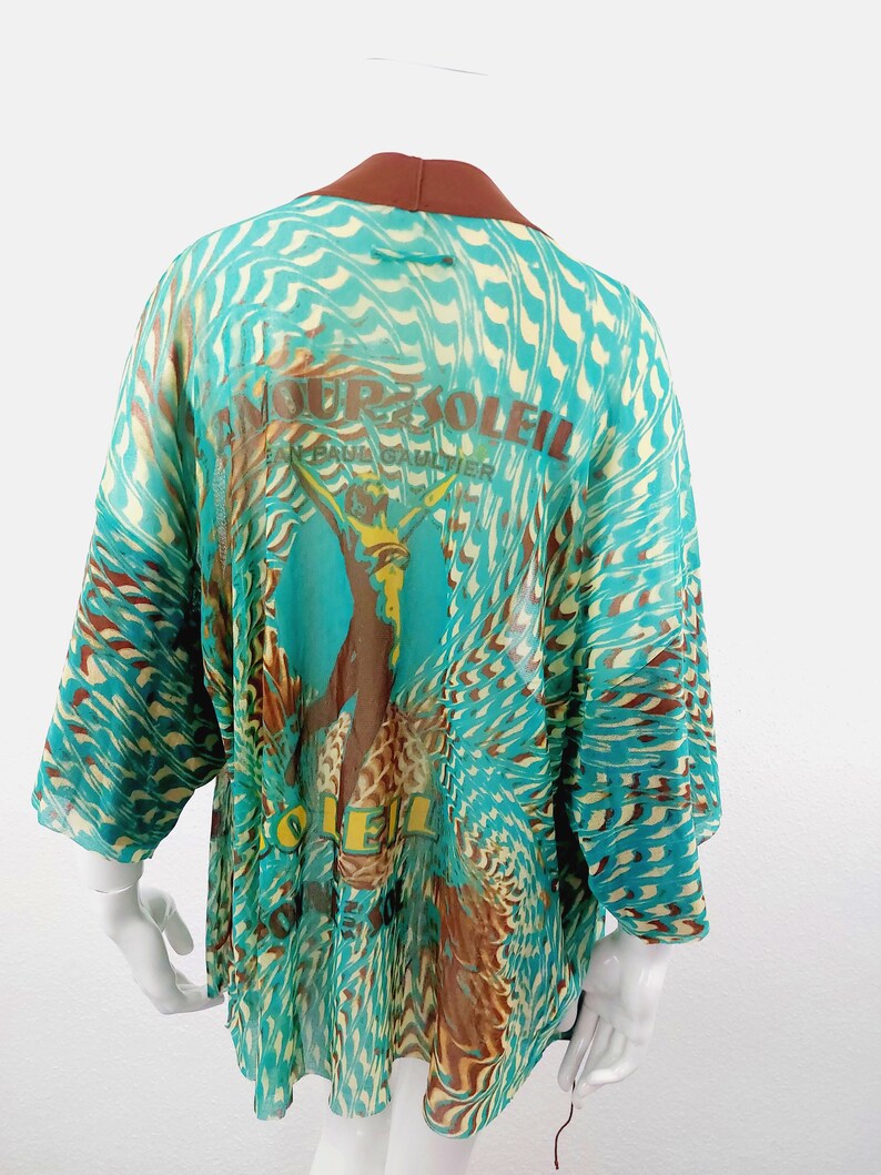May include: A turquoise and brown patterned sheer kimono with a brown collar and the text "Amour Soleil Jean Paul Gaultier" printed on the back.
