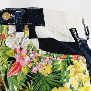 May include: Black and white checkered denim pants with a tropical floral print. The pants have a black waistband with the word "VERSACE" written on the back.