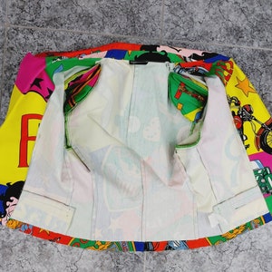 May include: A colourful jacket with a cartoon print featuring a motorcycle, a woman, and the word "FAME". The jacket is unzipped and the lining is white.
