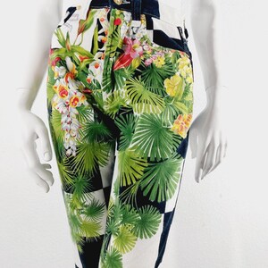 May include: Black and white checkered pants with a tropical floral print. The print features green leaves, yellow and red flowers.