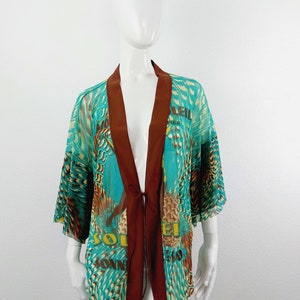 May include: A turquoise and brown patterned kimono with a tie closure. The kimono has a print of a bird and the text "Soleil" and "Montier" on it.