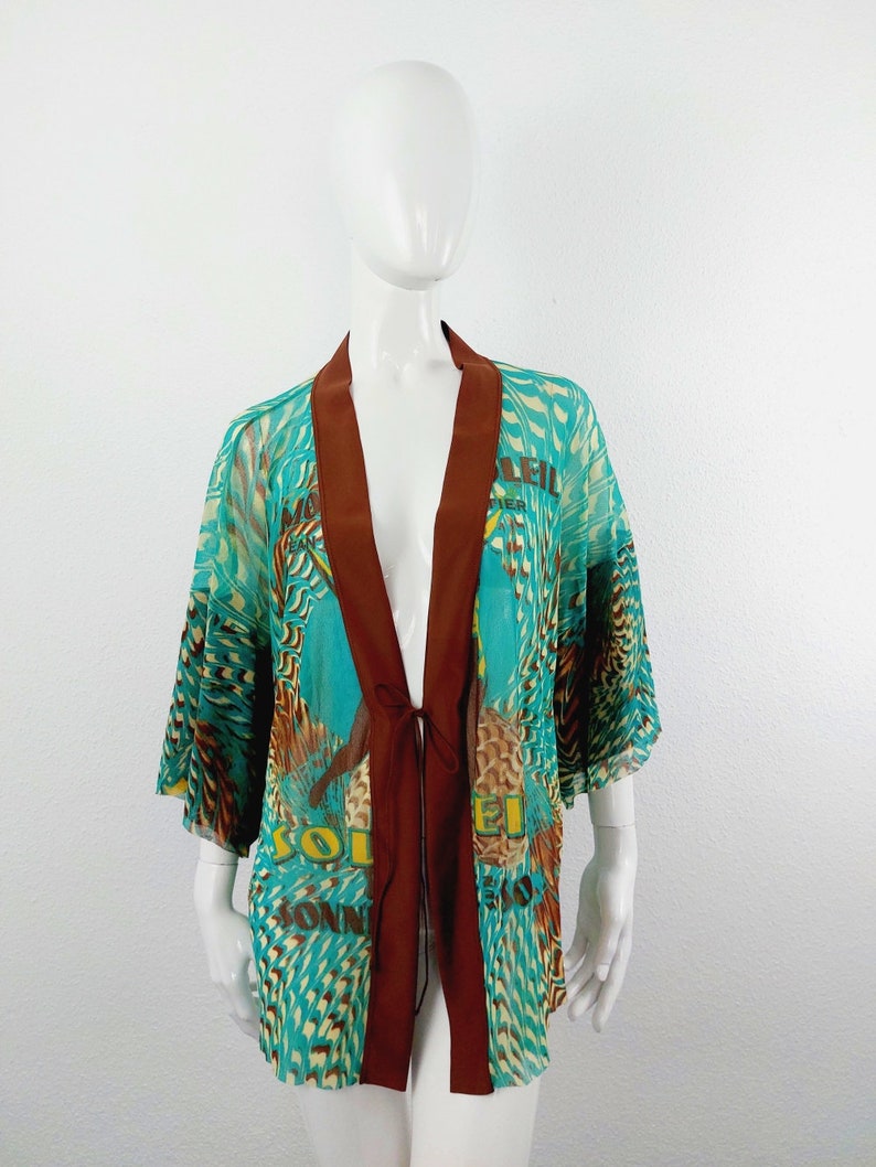 May include: A turquoise and brown patterned kimono with a tie closure. The kimono has a print of a bird and the text "Soleil" and "Montier" on it.