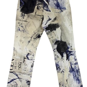 May include: White denim jeans with a blue and black abstract print. The print features a variety of shapes and lines, including a human eye and a hand.