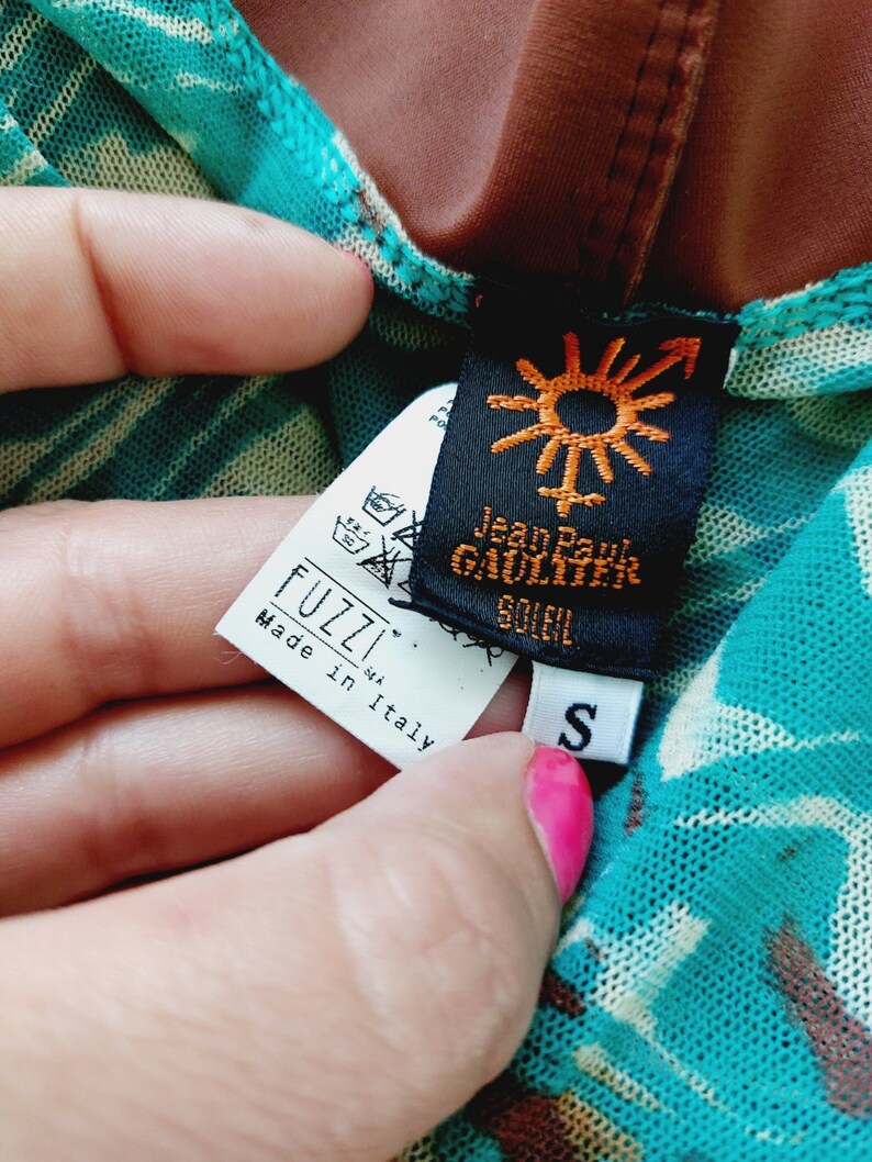 May include: A turquoise and brown patterned mesh top with a black tag that says "Jean Paul Gaultier Soleil" and a white tag that says "Fuzzi S.r.l. Made in Italy" and a white tag with the letter "S" on it.