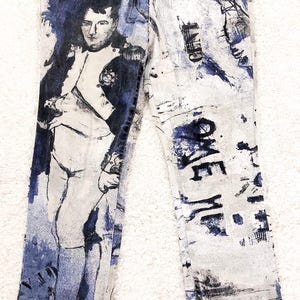 May include: A pair of blue and white jeans with a graphic print of a man in a military uniform and the word "ONE" on the right leg.
