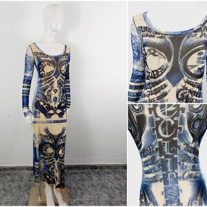 May include: A long, sheer, blue and cream-colored dress with a print of words and images. The dress has a scoop neck and long sleeves.