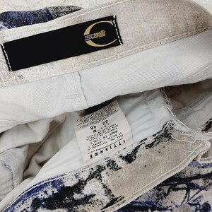May include: A white and blue patterned pair of jeans with a black label that says "Just Cavalli" and a white tag with the text "T.T.I.L.I.E.R.E.  CONA  P.T. TORNARE  MADE IN ITALY  D.I.  BOL.128  49  32  F.  4  PANTALONI  LAVAGGIO A FREDDO  NON CANDEGGIARE  STIRARE A BASSA TEMPERATURA  NON ASCIUGARE IN TAMBURO  LAVAGGIO A SECCO  CON PERCLORETIEN  "