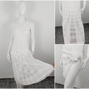 Può includere: Abito bianco senza maniche con colletto e design plissettato. L'abito ha un corpetto aderente e una gonna fluida.