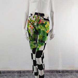 May include: Black and white checkered pants with a floral print on the top half. The floral print features green leaves, pink, yellow, and white flowers.