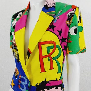 May include: A short-sleeved, multi-coloured blazer with a patchwork design. The blazer features a large "PR" logo in red and green letters on a yellow background. The blazer also features a cartoon character with black hair and a pink dress.