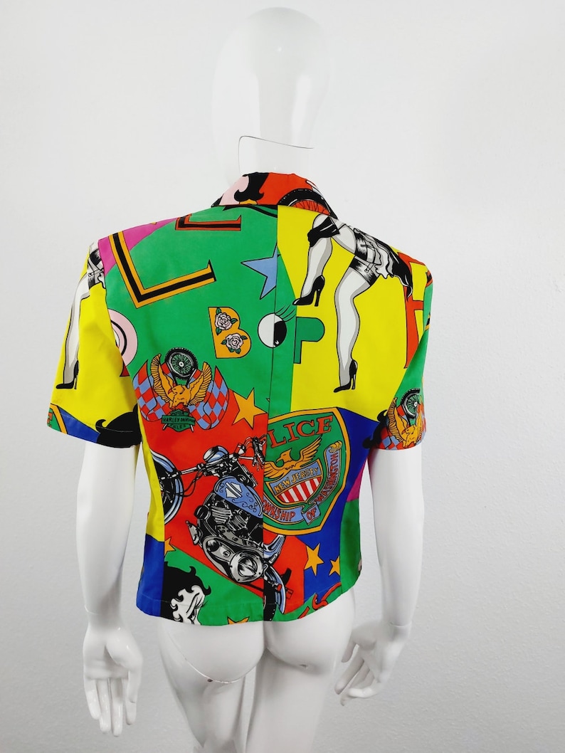 May include: A short-sleeved, multi-coloured button-up shirt with a bold, graphic print featuring a motorcycle, stars, and the words "Police" and "New Jersey".