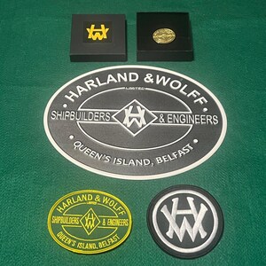 May include: An assortment of Harland & Wolff memorabilia, including a large oval sign, two small boxes, and two circular patches. The sign and patches feature the company logo and text. The boxes contain a gold-colored coin and a yellow logo.