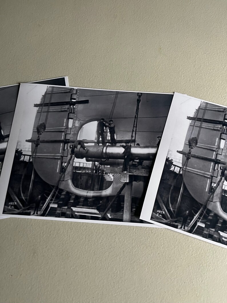 Pu&ograve; includere: Fotografia in bianco e nero di una grande nave in costruzione. Si possono vedere operai su impalcature, che lavorano allo scafo della nave. L'immagine &egrave; un primo piano della prua della nave.