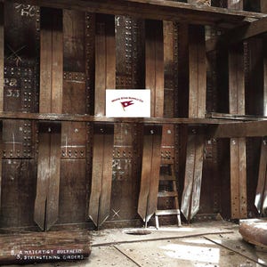 May include: An aged, interior view of a ship's hull, featuring wooden and metal structural components. The image shows a watertight bulkhead with strengthening girders. The White Star Supply Co. logo is visible. The scene is dominated by dark brown and metallic tones.